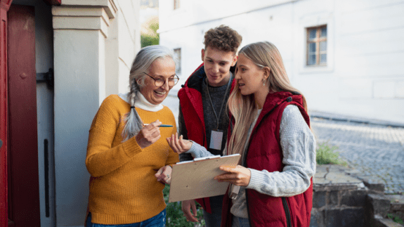 Two young people with clipboards speaking to an elderly lady