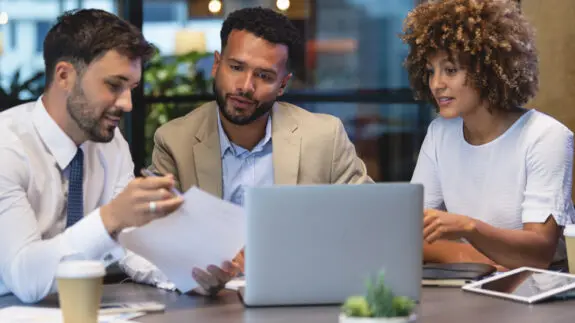 Three business people meeting and looking at a laptop and a document.