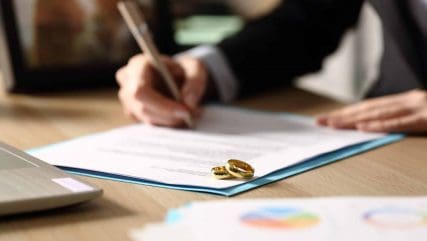 Close up of a person sitting at a desk signing a divorce legal document