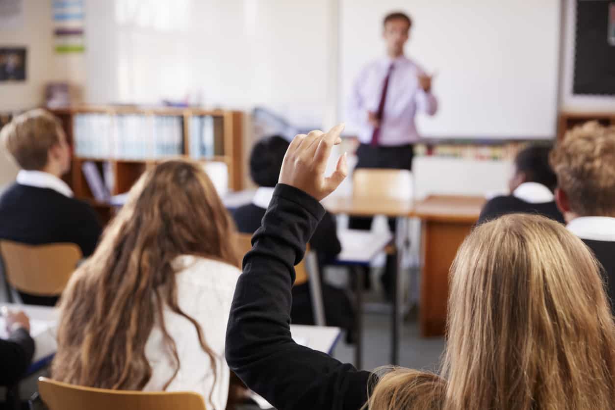 Children sitting in classroom with arms raised