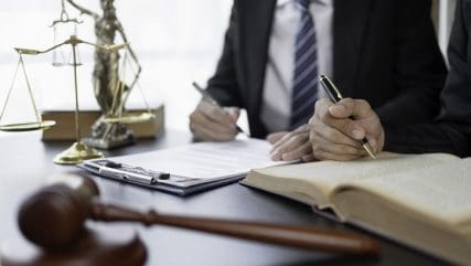 Two people sitting at desk writing in book