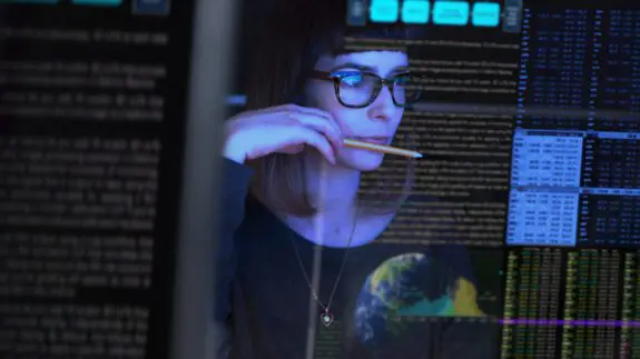 woman looking at data on a computer screen with reflections of data reflecting from glass