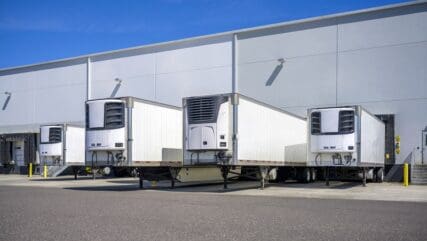 Refrigerator semi trailers without semi trucks standing at warehouse dock gates loading frozen cargo for next freight