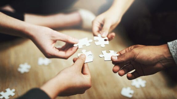 Four peoples hands holding puzzle pieces over a table