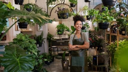 A cheerful woman wearing an apron while working in a plant shop, surrounded by an array of lush plants.