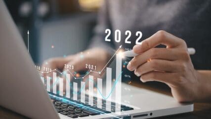 Someone is holding an interactive pen in their hand, pointing it towards the top of a laptop, up to the year 2022.