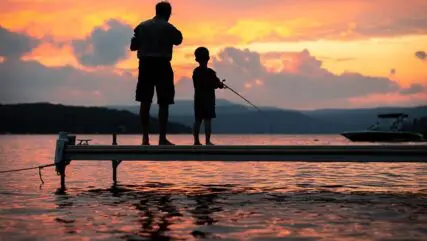 silhouette of a older man and child fishing on a dock at sunset