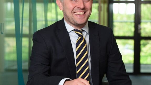 Michael Morter staff photo sitting a desk smiling