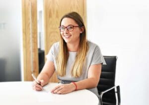 Zoe Masterton sitting at desk holding a pen and smiling