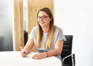 Zoe Masterton sitting at desk holding a pen and smiling