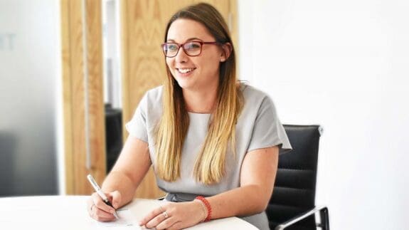 Zoe Masterton sitting at desk holding a pen and smiling