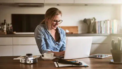 Woman sitting in kitchen reading on laptop