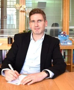 Jon Chambers sitting in office at a desk holding a pen