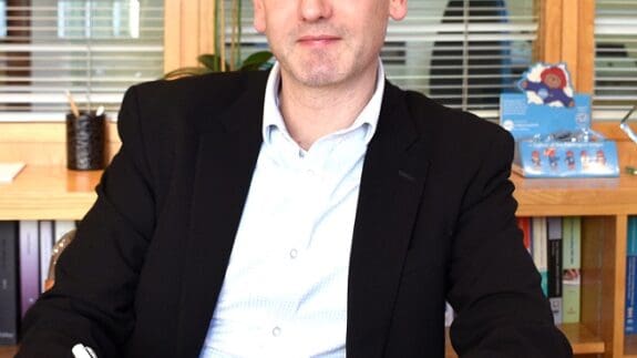 Jon Chambers sitting in office at a desk holding a pen
