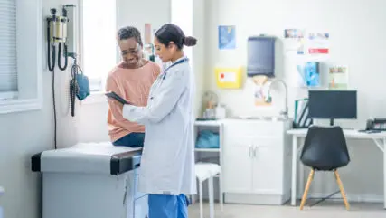 Doctor looking at a chart with a patient in a medical room.