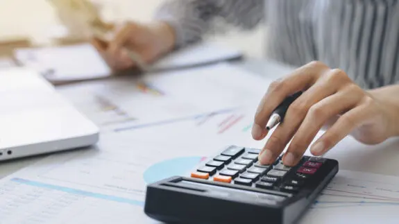 person sitting at desk with papers and calculator checking figures