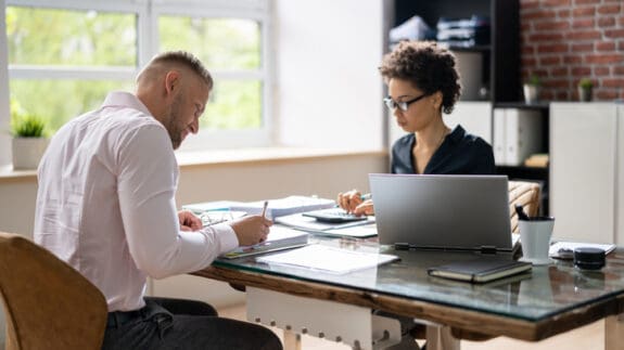 Two Business Colleagues Calculating Tax In Office