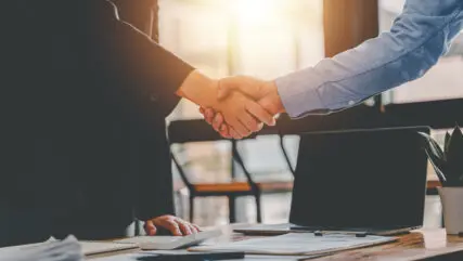 Two people shaking hands across a desk