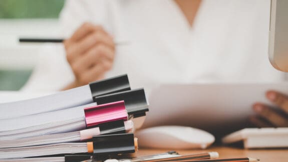 Woman checking work documents with unfinished stack of document paperwork holding a pen