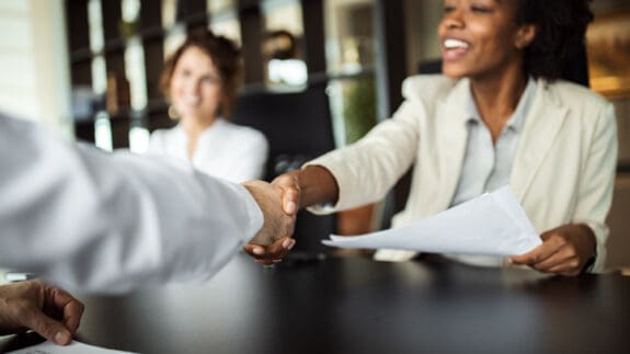 over shoulder view of people sitting at office table an arm shaking a womans hand