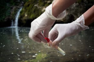 White gloved hands collecting a water sample from a body of water.