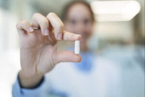 Doctor holding up a white capsule pill.