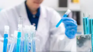 Scientist in background holding up a test tube with blue liquid inside.