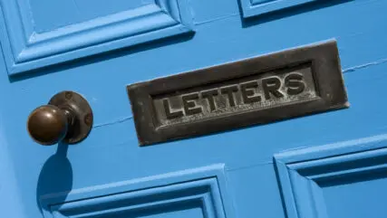 Close up of a bright blue door with an aged metal letterbox.