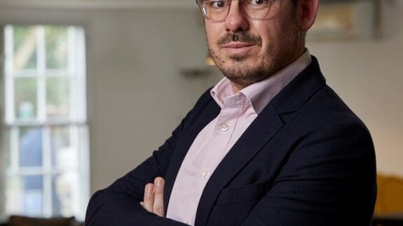 Tom Meeks standing in office smiling with arms folded