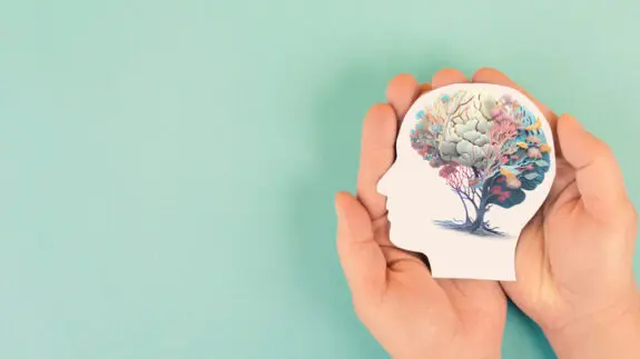 Hands holding paper head, human brain with flowers, self care and mental health concept, positive thinking, creative mind