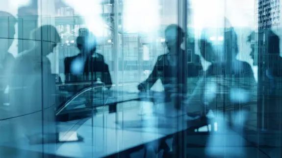 Blur image of a group of professionals sat around a table surrounded by glass doors.