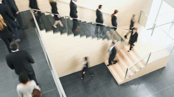 Blurred office workers walking up and down stairs, representing movement in employment and taxation of termination payments