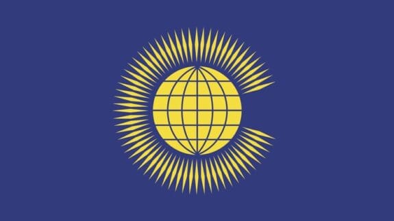 The flag of the Commonwealth - a dark blue background with a yellow globe in the centre surrounded by thin yellow diamonds.