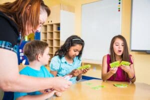 Teacher helping students sitting around a desk to play a card game.
