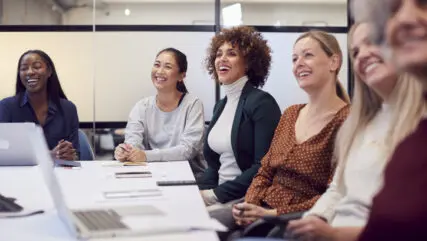 Business women around a table in the boardroom, laughing and conversing.