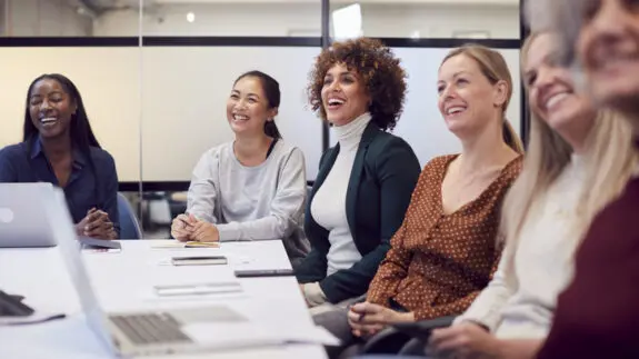 Business women around a table in the boardroom, laughing and conversing.