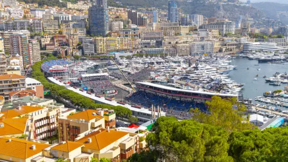 View from the Rock of Monaco of the Grand Prix race track, city skyline, mountains and harbor filled with luxury yachts in Monte Carlo, Monaco.