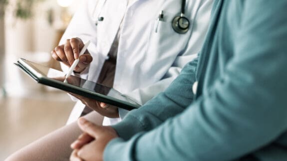 Doctor, hands and tablet with patient for consultation, medical advice or procedure at clinic. Closeup, healthcare employee and client with technology for health appointment or checklist at hospital