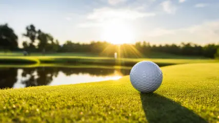 White Golf Ball On Picturesque Green Golf Course At The Sunset.