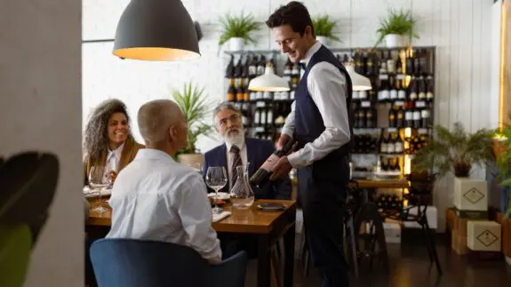 Waiter serving wine to business diners in an upscale restaurant, highlighting quality customer service