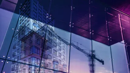 Construction crane and a new high rise building reflected into a newly built office building. New offices are being built to satisfy the growing demand