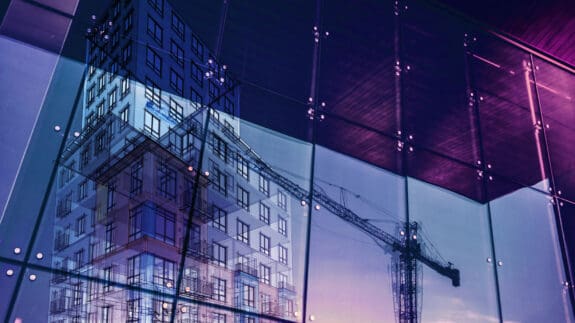Construction crane and a new high rise building reflected into a newly built office building. New offices are being built to satisfy the growing demand