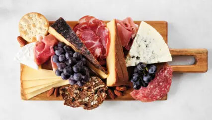 Charcuterie board of assorted cheeses, meats and appetizers. Top view on a white marble background.