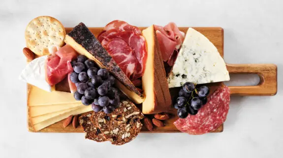 Charcuterie board of assorted cheeses, meats and appetizers. Top view on a white marble background.