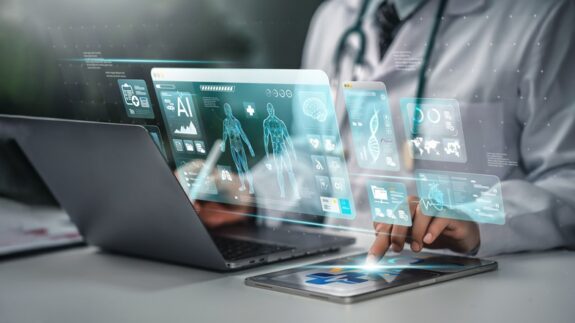 A doctor using a tablet and a laptop, with a holographic overlay showing a human body, DNA, and reports.